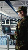 Vertical Soldier in engineering role uses AI application on laptop to manage server hub systems. Army commander reviews secret intelligence information using artificial intelligence in data center, camera A video