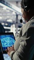 Vertical Server room tech support employee using AI on tablet to guide clients. Technician in data center helps users fix system errors on servers using artificial intelligence, camera B video
