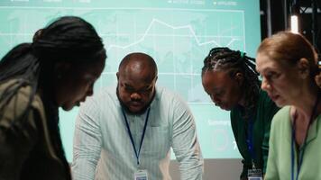 multi-etnisch team uitwisselen bestanden en recensie voorspelling diagrammen Bij nacht, vergadering in een stil kantoor ruimte. na uren samenwerking naar bereiden sleutel project updates voor aandeelhouders. camera b. video