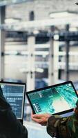 Vertical Army commander and software developer in data center integrating AI into radar systems for missile tracking. Soldier and female programmer in server hub analyzing aerial movement on laptop, camera B video