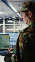 Vertical Military technician in data center tracking satellite coordinates using notebook software interface. Army unit in server hub analyzing reconnaissance data through satellite imaging systems, camera A video