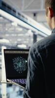 Vertical Software developer in data center checks AI dashboard using laptop during routine systems review. Server hub IT specialist tests artificial intelligence on notebook to check performance, camera B video