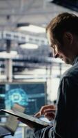 Vertical Jolly IT professional monitors server room activity using tablet in facility. Happy data center technician reviews rigs tests results with device to ensure systems are working correctly, camera B video