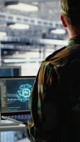 Vertical Army programmer in high tech server hub uses AI application on laptop to review reconnaissance information. Data center IT expert wearing military uniform uses AI on notebook to plan mission, camera B video