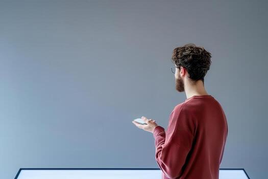 Man holding smartphone wearing red sweater with gray background and modern table photo