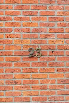 Metal house number twenty three fixed on a red brick wall indicating the address of a building, providing information and guidance for visitors and residents, photo