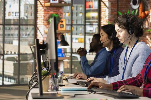 Team of multiethnic call center workers dealing with upset customers, speaking using headset at office desk. Multiracial colleagues doing customer support job in workplace, handling clients complaints photo