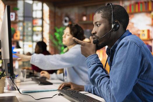 Call center employee dealing with upset customers, speaking with them using headset at office desk. Man doing customer support job in workplace handling clients complaints photo