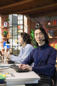 Portrait of senior call center agent typing on PC keyboard, assisting customers through digital communication channels. Experienced Asian customer support employee conversates with client in live chat photo