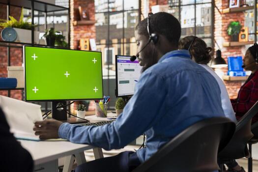 Call center admin at green screen PC desk reading paperwork, learning to improve customer loyalty. Customer support worker using mockup computer, looking over documentation photo