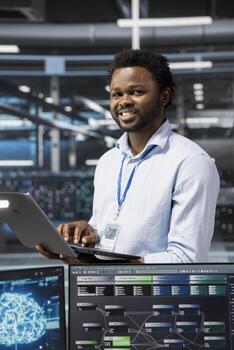 Portrait of smiling engineer in data center using artificial intelligence computerized model. Happy server room IT professional working with AI machine learning algorithms photo