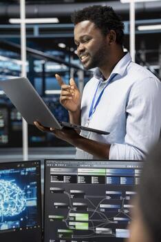 contento datos centrar técnico utilizando ordenador portátil dispositivo a visualizar artificial inteligencia neural redes alegre hombre en servidor habitación mirando a cuaderno mostrar, supervisando ai sistemas foto