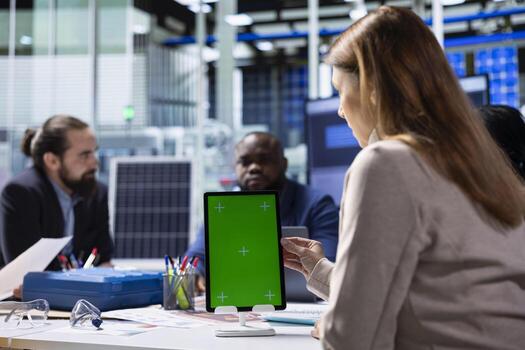 Photovoltaics factory workers analyzing data, reviewing system health metrics with isolated screen tablet. Solar panels plant employees troubleshooting technical issues using mockup device photo