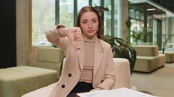 disgusto. trastornado caucásico mujer de negocios sentado en oficina vestíbulo demostración pulgar abajo firmar gesto, expresando descontento, desaprobación insatisfecho malo trabajar. disgustado grave persona de libre dedicación en formales. video