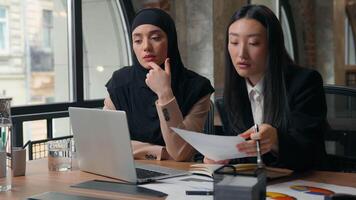 dois multirracial o negócio mulheres fêmea colegas empregadores multiétnico mulheres de negócios ásia mulher muçulmano menina concentrado resolução corporativo trabalhos problema discutir com computador portátil documento às escritório mesa video