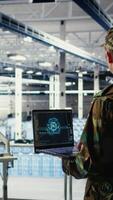 Vertical Army programmer in high tech server hub uses AI application on laptop to review reconnaissance information. Data center IT expert wearing military uniform uses AI on notebook to plan mission, camera A video