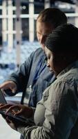 Vertical Server room coworkers use laptop to install updates and keep AI systems running. Data center engineering team uses notebook to write code improving infrastructure output, camera B video