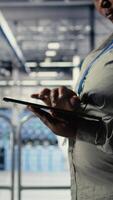 Vertical Data center programmers check AI dashboard using tablet, doing systems review. Server hub coworkers test artificial intelligence tools on device to ensure reliable performance, camera A video