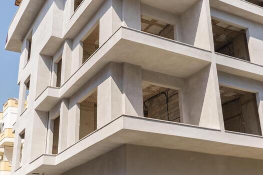 A contemporary structure features sharp lines and large windows at different levels, reflecting modern architecture. The building is in the early stages of construction under a clear blue sky photo