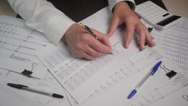 In a business setting, hands are focused on filling out financial reports with documents scattered across the desk, emphasizing productivity and attention to detail. photo