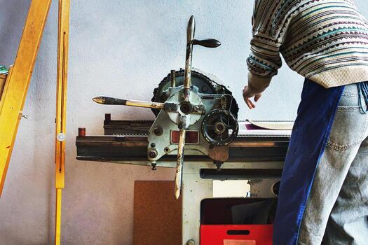 A printmaker in the patterned sweater and apron operates a traditional mechanical printing press. Back view of the artist during the printmaking process photo