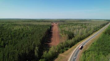 fuco aereo Visualizza di un' autostrada con camion guida vicino un' nuovo strada sotto costruzione attraverso un' foresta, presto per Collegare con il esistente autostrada, su un' soleggiato giorno. video