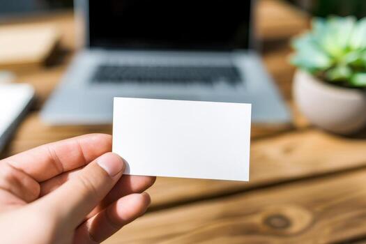 a Hand holding blank business card mockup in cozy workspace with notebook. White card template against marble table background. Perfect for branding presentation, photo