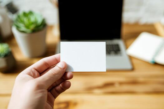 Hand holding blank business card mockup in cozy workspace with notebook. White card template against marble table background. Perfect for branding presentation.. photo