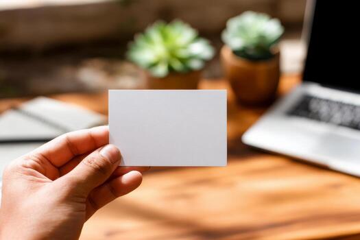 Hand holding blank business card mockup in cozy workspace with notebook. White card template against marble table background. Perfect for branding presentation. photo