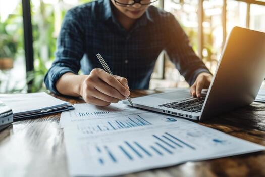 Man working on laptop with papers and pen photo