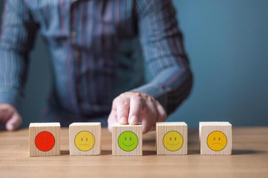 A hand selects a smiling face block among various emotion blocks, representing customer satisfaction and feedback. photo