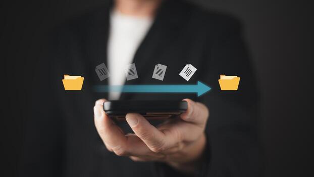 A person holds a smartphone displaying a digital transfer of documents between yellow folders, symbolizing seamless file sharing, document management, and efficient digital organization. photo