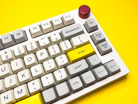 White mechanical keyboard with Enter key on bright yellow background, keyboard buttons. A keyboard with a yellow key on the bottom left photo