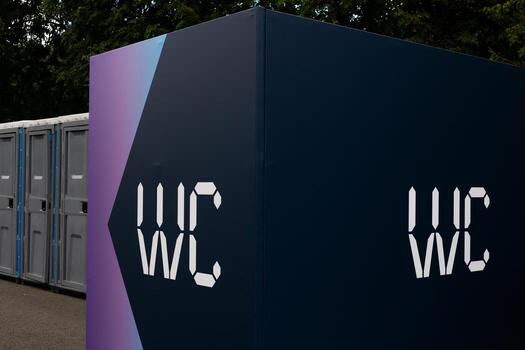 Portable WC sign on modern toilet container with purple gradient background in urban environment. Portable restroom in construction area or outdoor event, temporary sanitation solution photo