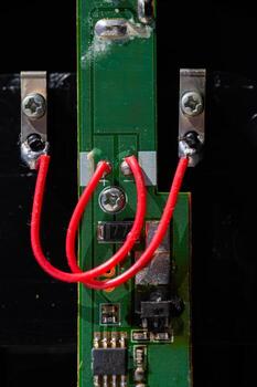 A detailed, vertical macro shot of a green printed circuit board PCB with a red wire soldered to two points. The image captures electronic components and intricate circuitry details. photo