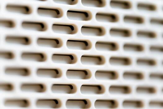 A macro close-up of a white perforated plastic surface. The pattern of horizontal oval openings arranged in staggered rows is shown with a shallow depth of field, highlighting the texture. photo