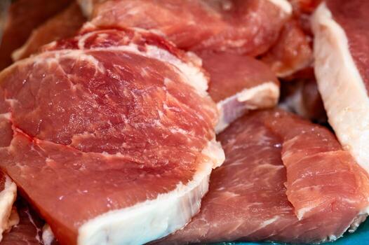 A macro of several pieces of raw, fresh pork meat. The image captures the detailed texture of the muscle tissue and the white fatty layers, with a shallow depth of field. photo