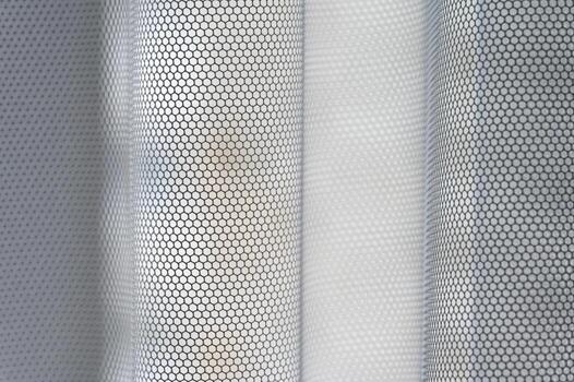 A macro close-up of a white fabric with a repeating hexagonal mesh pattern. The material is shown with soft folds, creating a sense of depth and a textured, abstract visual. photo