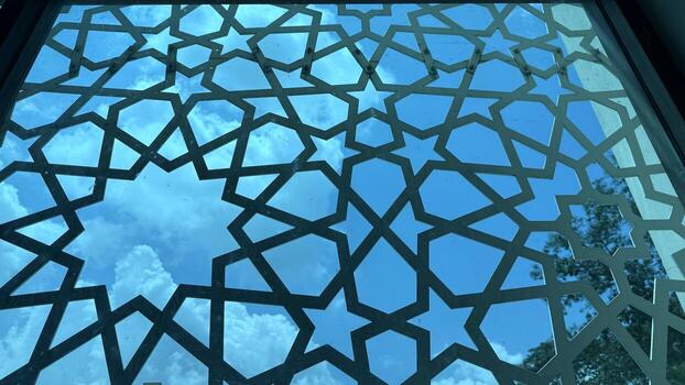 Ornate geometric metalwork frames blue sky with soft clouds creating a beautiful high resolution photo