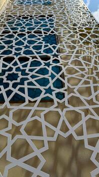 White geometric lattice pattern adorns a building facade obscuring windows viewed from a low angle photo
