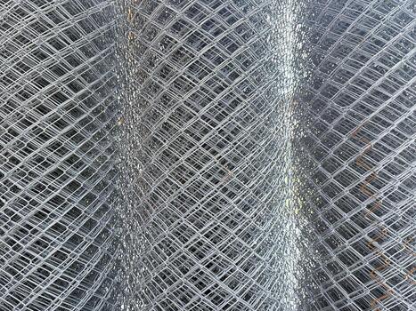 Stacked galvanized chain link fence roll shows a repeating diamond pattern, ready for security photo