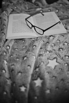 Cozy Reading Scene with Open Book and Glasses on Star Patterned Blanket in Black and White Ambiance photo