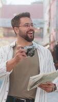 caucásico joven hombre turista de viaje en fines de semana explorador pueblo mirando ciudad mapa, haciendo foto imágenes en retro Clásico cámara al aire libre. contento adulto chico viajero en urbano ciudad calle. estilos de vida video