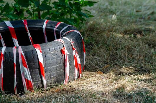 A tire is covered in red and white tape. The tire is on a patch of dry grass photo