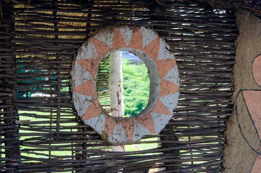 A small window with a wicker frame and a circle painted on it. The circle is surrounded by a pattern of triangles photo
