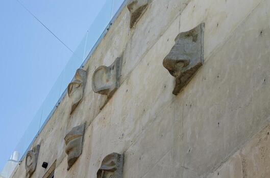 The wall is made of stone and has a lot of small holes in it. The holes are arranged in a pattern that looks like faces. The wall is also covered in a lot of concrete photo