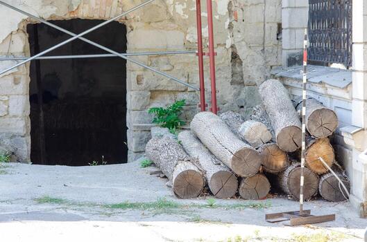 A pile of logs is stacked next to a building. The logs are old and weathered, and the pile is quite large. The scene has a rustic and natural feel photo