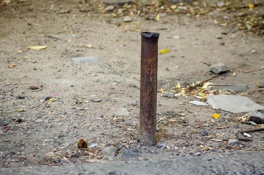 A rusty metal pole is standing in the dirt. The pole is bent and twisted, and it is broken. The image has a sense of decay and abandonment, as the pole is surrounded by debris and trash photo
