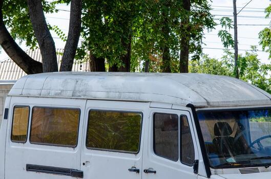 A white van with a dirty roof and windows. The van is parked in a parking lot. Scene is somewhat gloomy and dirty photo
