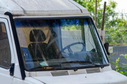 A dirty white van with a dirty windshield. The windshield wipers are on and the wipers are moving photo